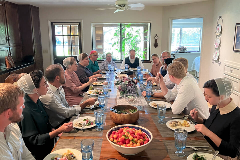 Guests and friends eat a Sunday meal together at a long table.