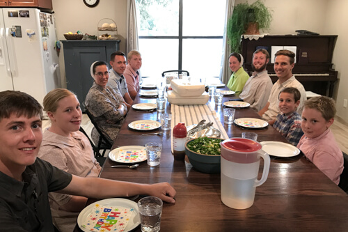 A large family sitting at a dinner table ready to eat.