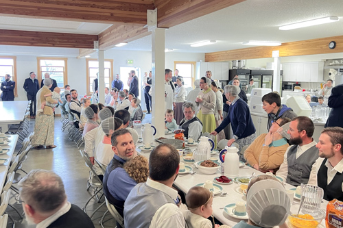 A large group of church members sit at a long table to enjoy a lovefeast lunch.
