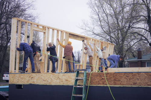 On a winter day, young men push a framed wall for a new house into place.
