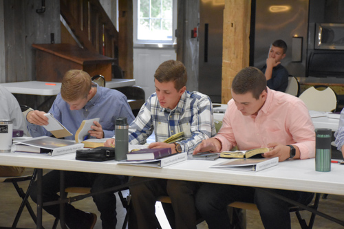 Three young men sit at a table, searching through their Bibles and taking notes.