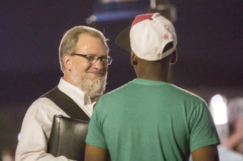 In the evening air, a man holding a Bible has a conversation with a younger man.