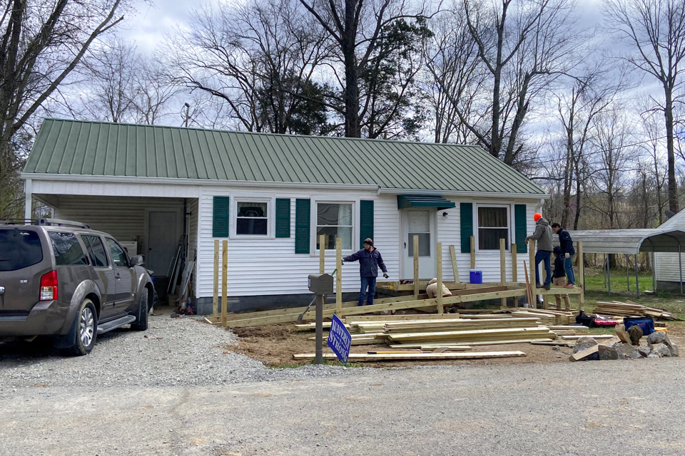 Three men construct a wooden ramp that stretching from a house's door down to the driveway.