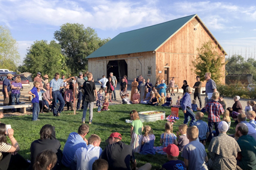 A ring of spectators sit in the evening sun and watch an activity in the center that involves a tub of apples