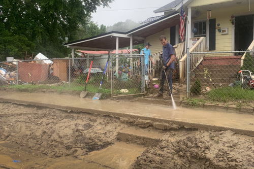 A young man power washes the mud off of a home's entry walk after a flood.