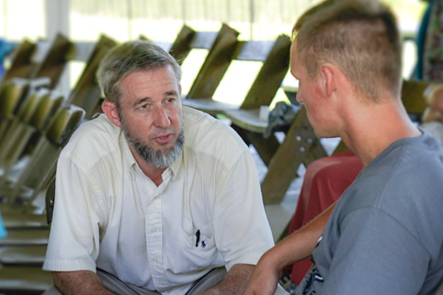 A man sits with a younger man and carries on a thoughtful conversation with him.
