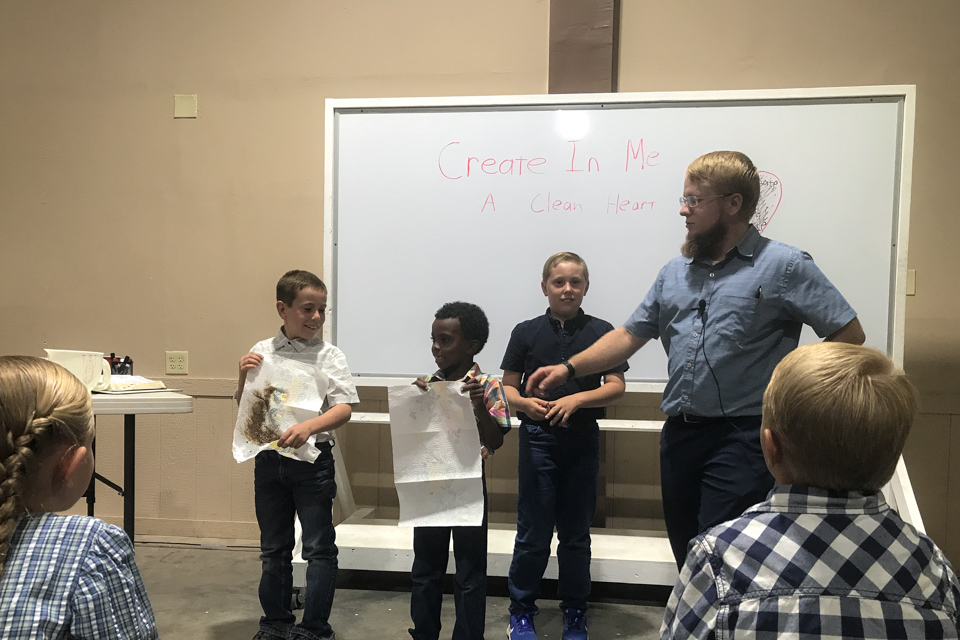 A man instructs young boys as they participate in an exercise during the man's talk.