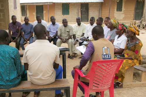A group of foreign church members sit around and discuss biblical teachings from a handbook.