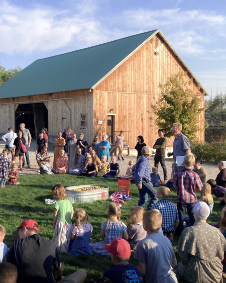 A ring of spectators sit in the evening sun and watch an activity in the center that involves a tub of apples