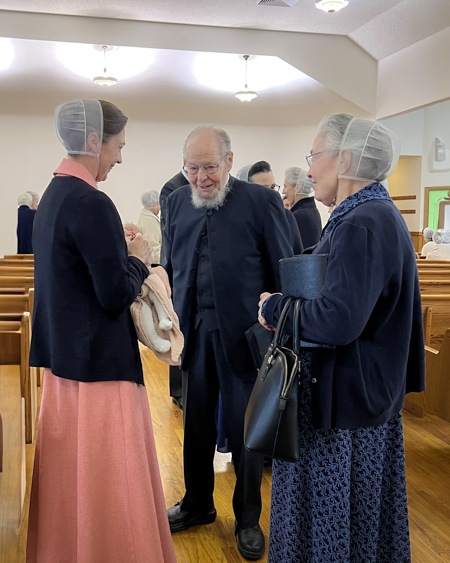 An elderly man talks with two women in a church's sanctuary after a service.