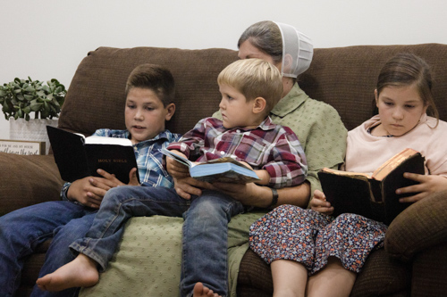 Three children and their mother sit on a couch as they read their Bibles for family devotions.