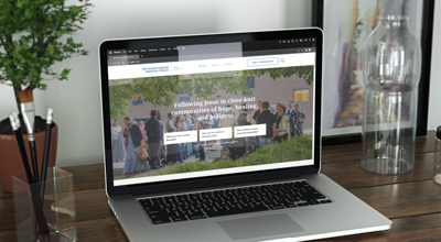 The German Baptist website home page is featured on an open laptop that sits on a wooden desk.