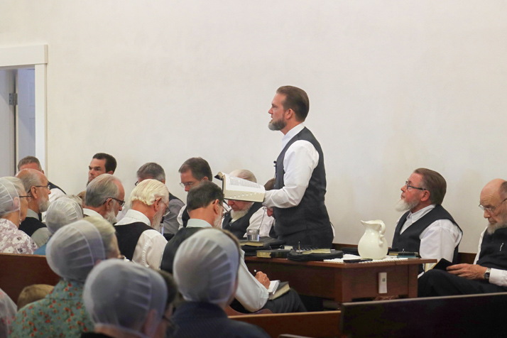 A preacher stands before a congregation and preaches from the Bible.