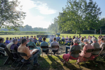 On a bright summer morning, a large group of young people sit around a campfire and read their Bibles.