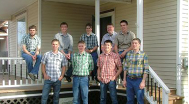9 young men participating in the CASP pilot project pose in front of a house.