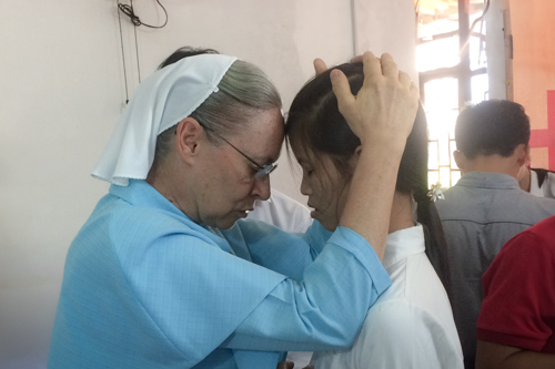 A woman places her hands on a young girl's head and their foreheads touch as the woman prays with her.